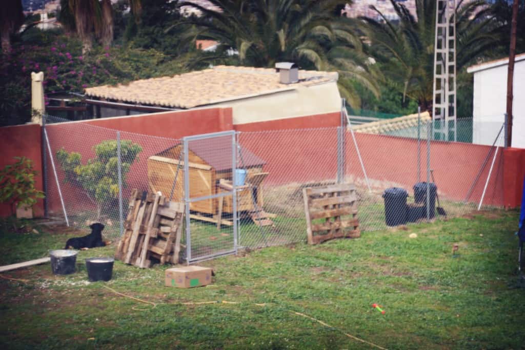 A chicken coop surrounded by a 2m high chain link fence.