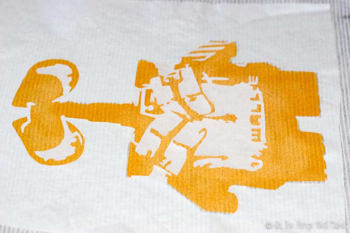 Close up of Wall-E freezer paper stencil ironed onto a t-shirt that already has a yellow painted layer on.