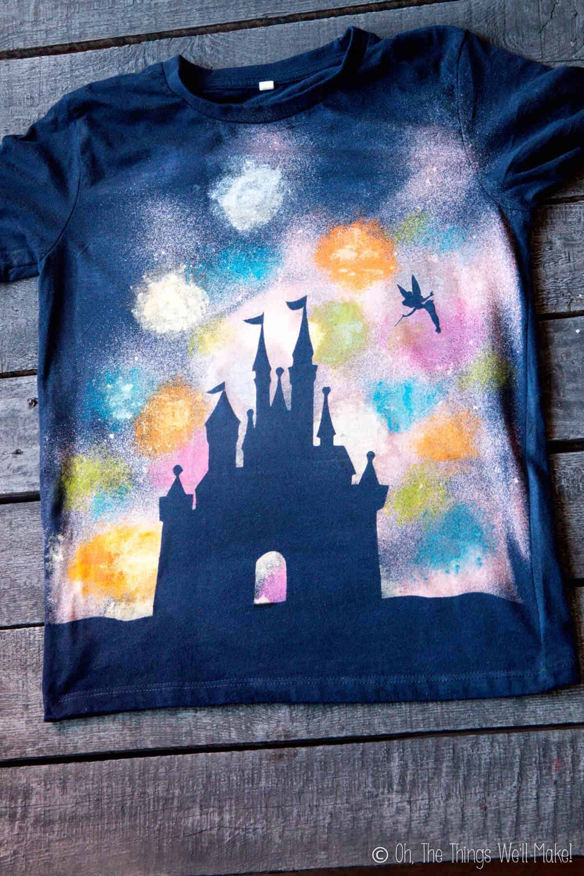 Navy blue t-shirt featuring a silhouette of the Disney castle and Tinkerbell flying on a colorful painted fireworks background.