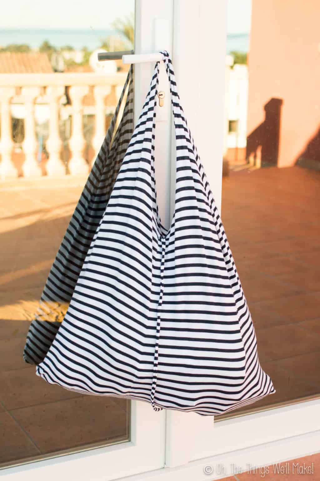 Finished striped white and black t-shirt bag hanging on a white glass door outside.