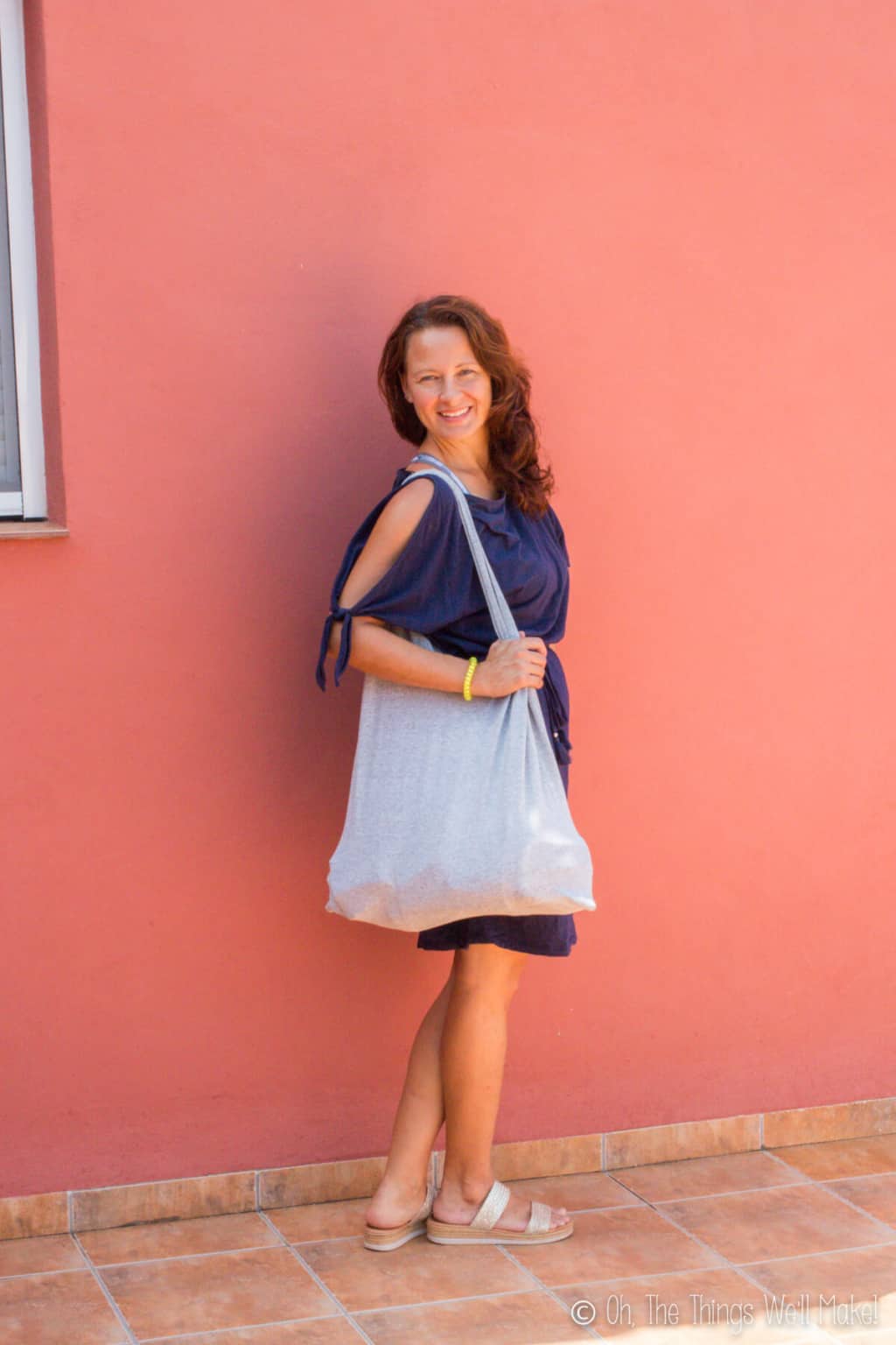 A caucasian woman smiling wearing a navy blue dress showing off her handmade striped t-shirt bag.