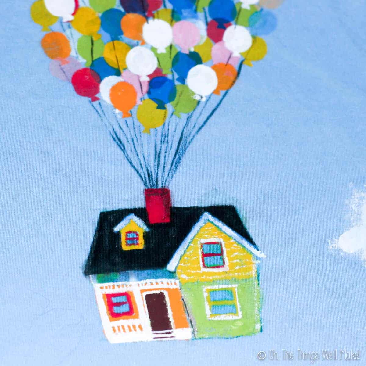 Closeup of the colorful "Up" house painted on a blue t-shirt with balloons pulling it up.