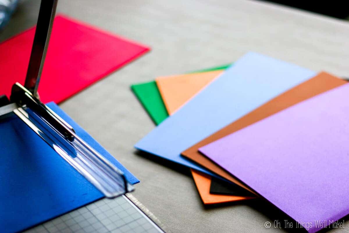 Several pieces of colorful craft foam on a table with a paper cutter on the side.