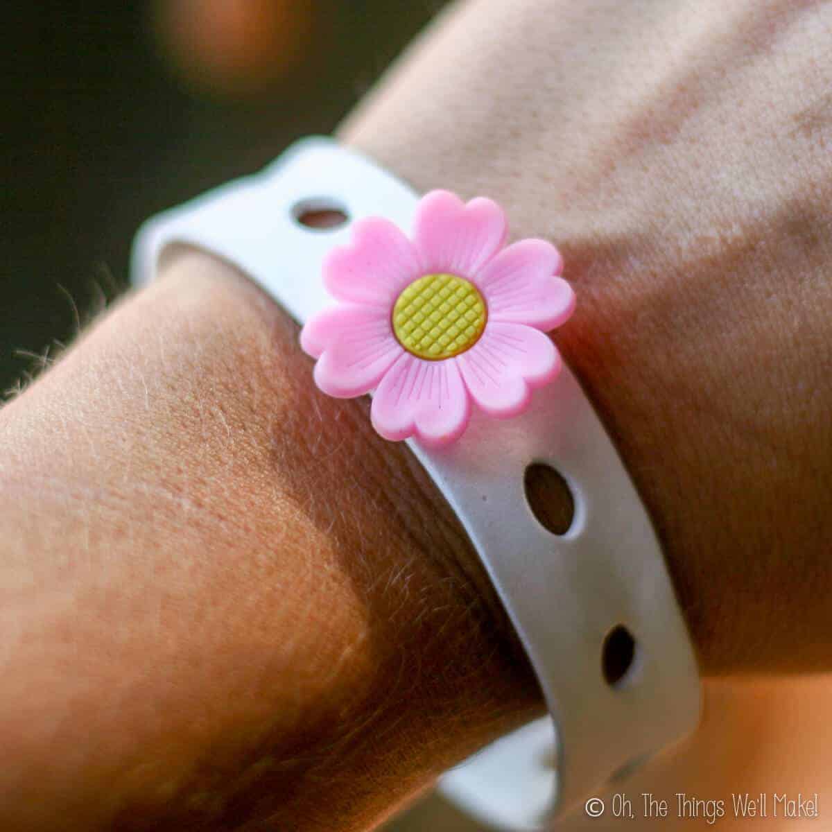 Close up of a wrist wearing homemade white craft foam bracelet with a pink petal, yellow center flower charm.