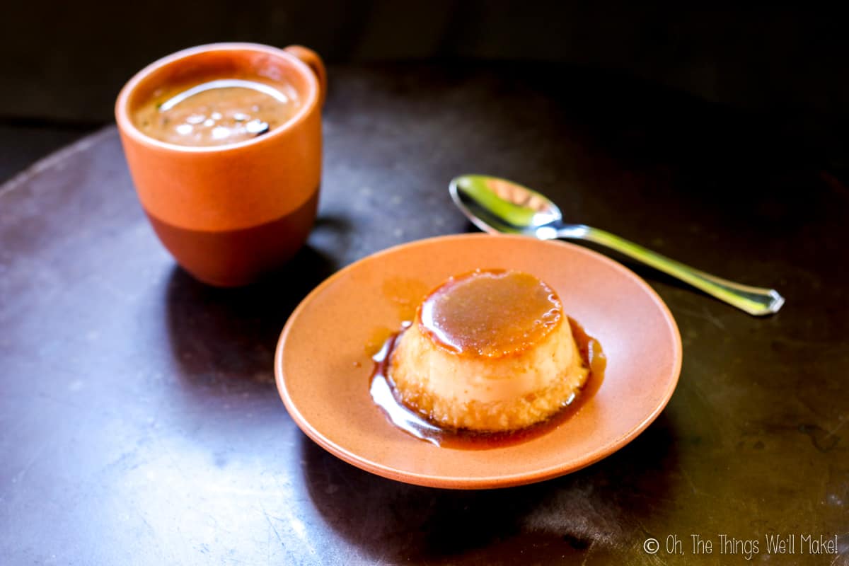 Homemade coconut flan on an orange plate with a silver spoon beside it and a cup of coffee on the other side.