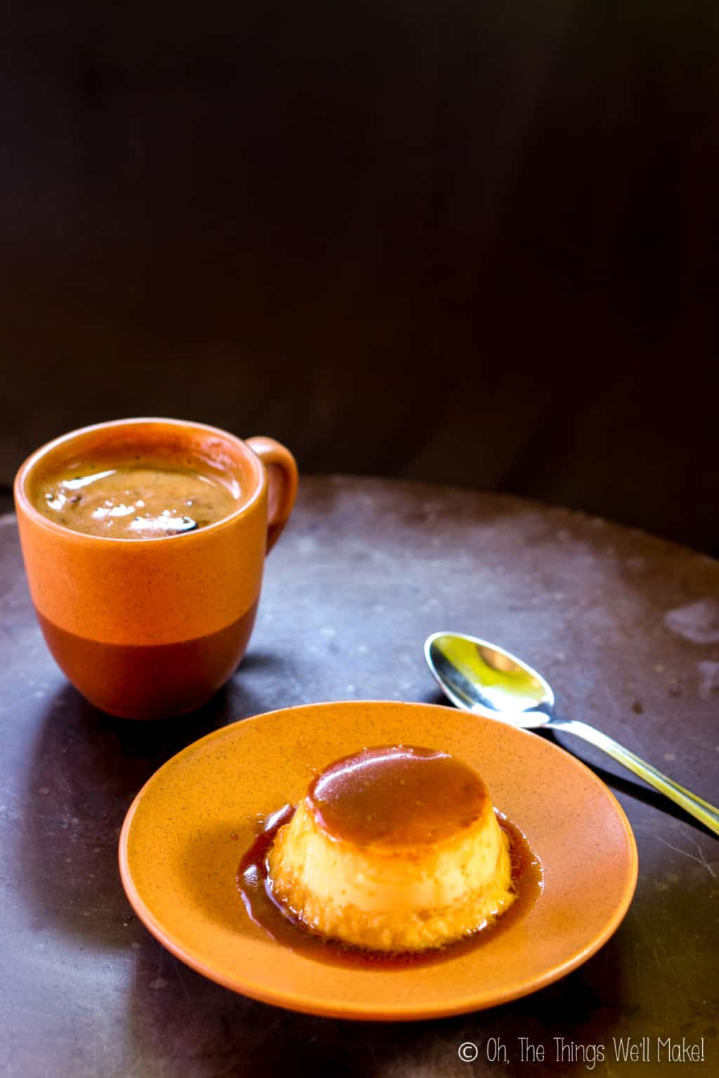 Homemade coconut flan on an orange plate with a silver spoon beside it and a cup of coffee on the other side.