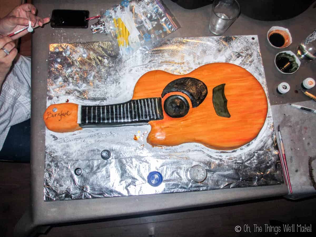 Top view of a fondant guitar cake with someone making tuning keys out of fondant on the left side
