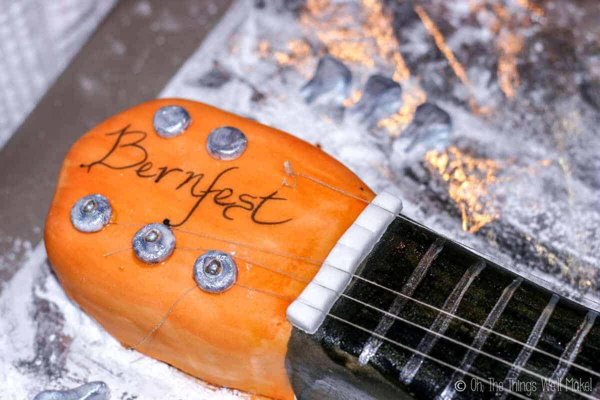Close up of head of the guitar cake with handmade fondant tuning keys in silver with the words "Bernfest" written on the center.