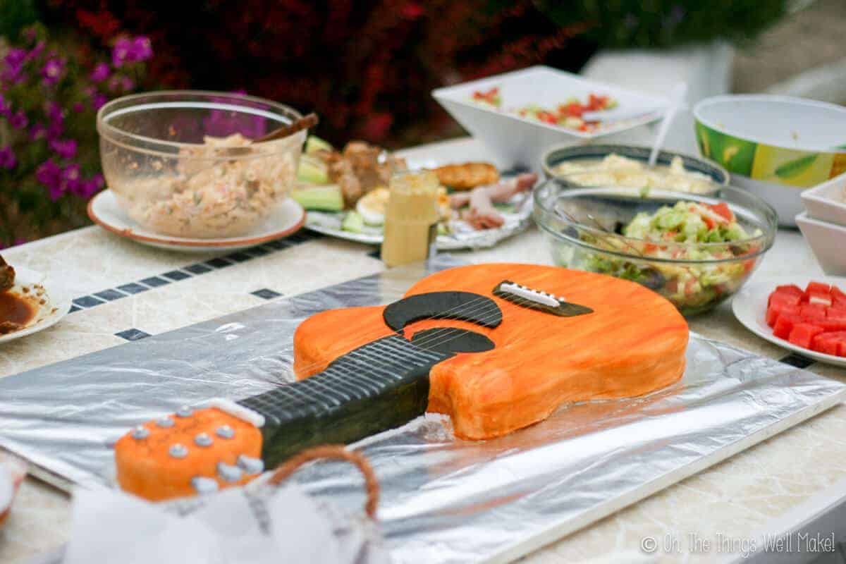 A full spread of food on a table with a orange guitar fondant cake as focus.