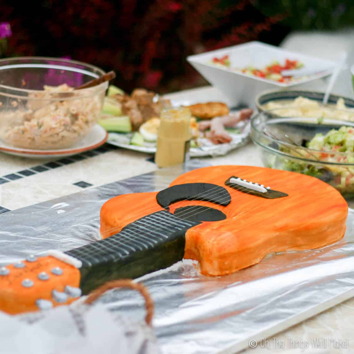 A full spread of food on a table with orange guitar fondant cake as focus.