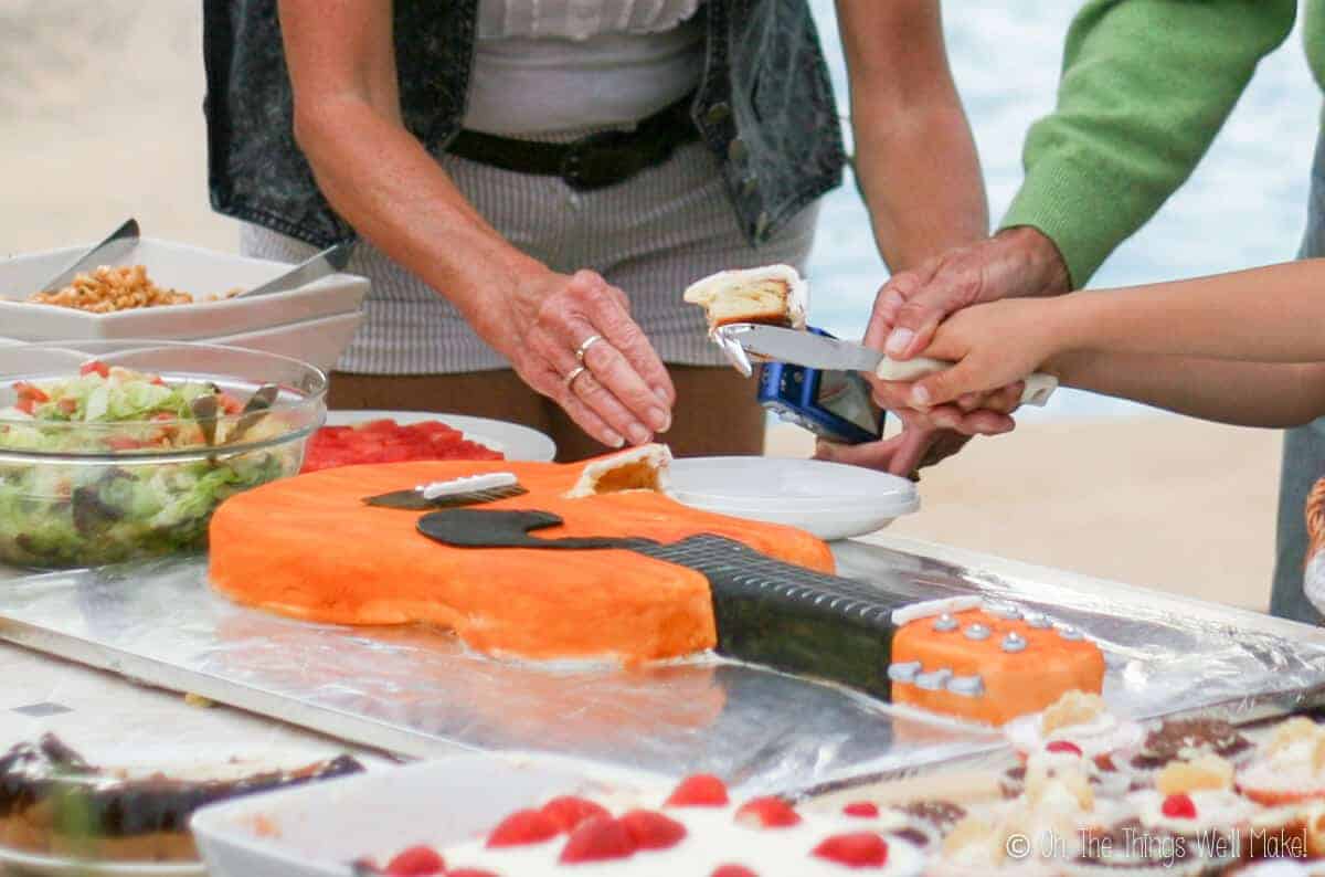 Several hands reached out to cut the orange guitar cake