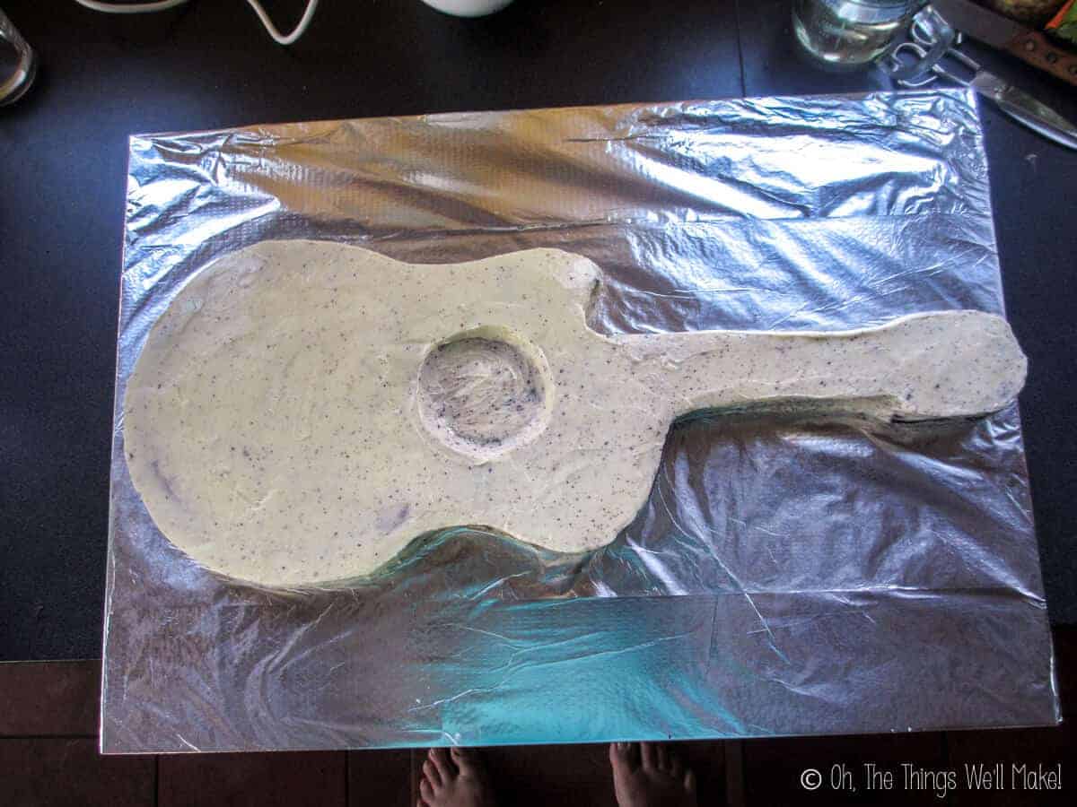 A guitar shaped cake covered in more white buttercream frosting.