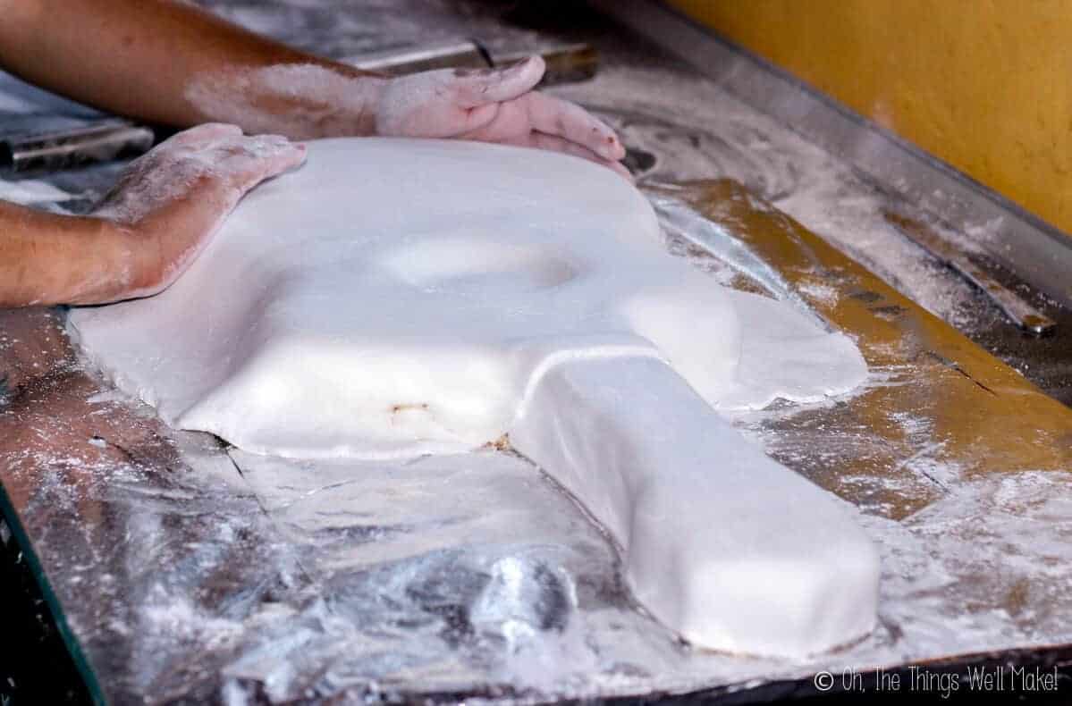 Side view of two hands shaping white fondant placed over the guitar shaped cake.