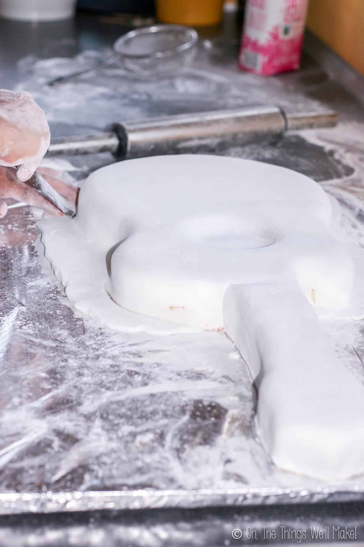 Side view of two hands cutting the excess fondant off the guitar cake.