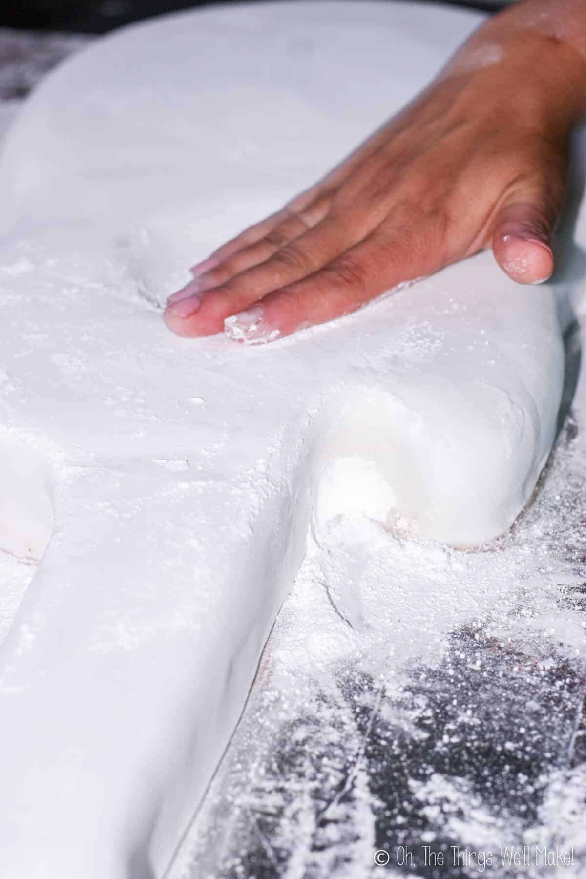 Close up of a hand rubbing the seams between the fondant sheets with powdered sugar all over the fondant.