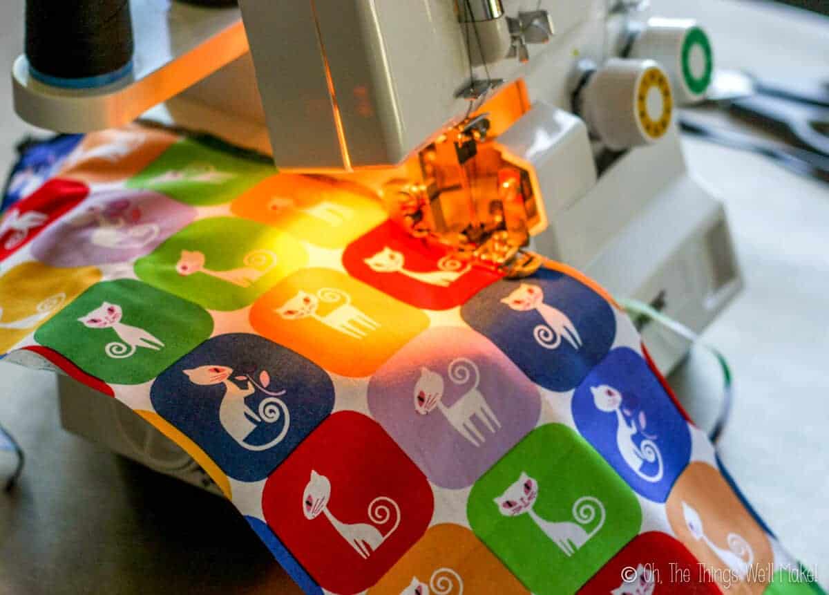 Close up of a colorful cat print cloth going through a serger machine.