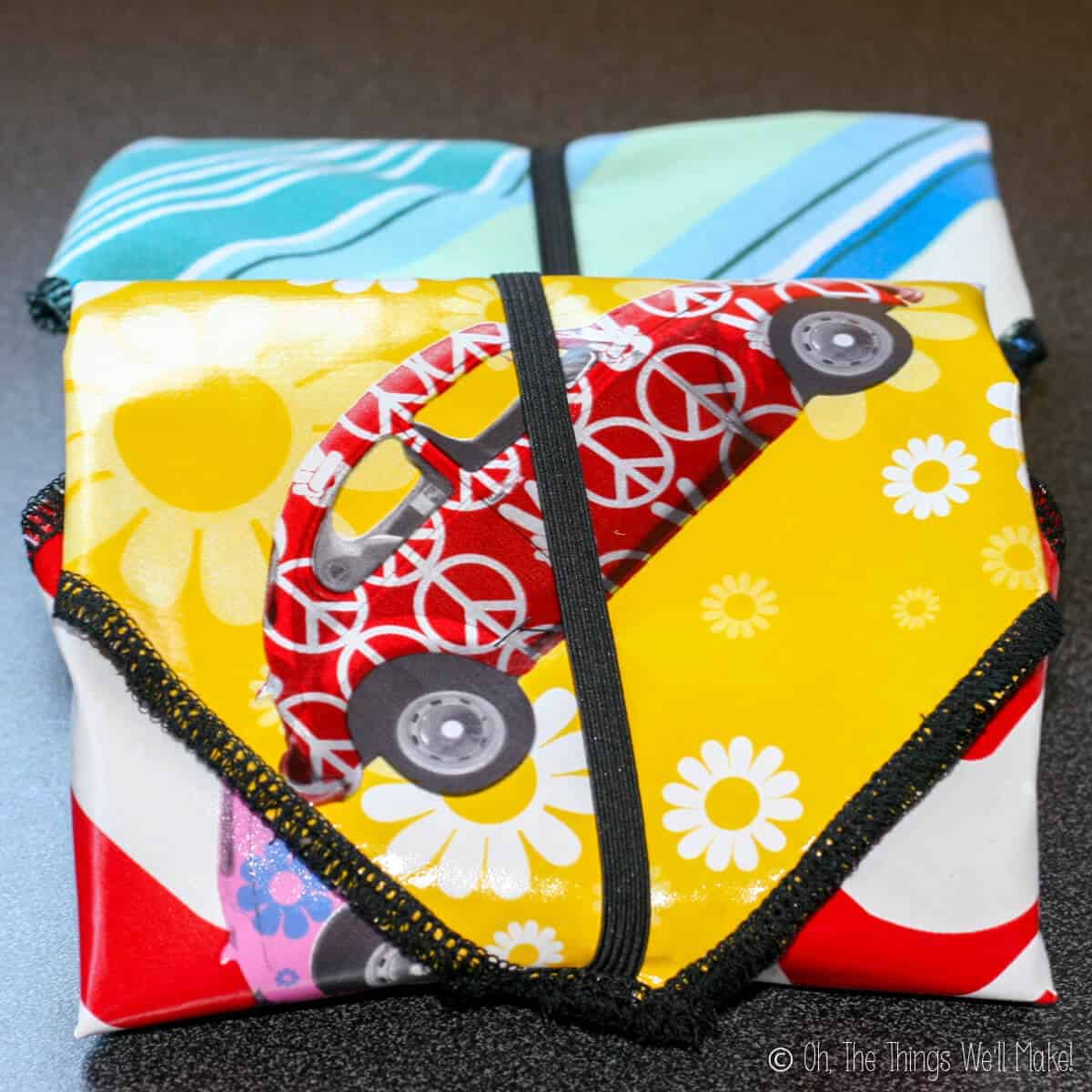 Closeup of two colorful sandwich wraps. One in front has a red Volkswagen Beetle print in a yellow, white floral design, and red fabric. Snack bag in the back is blue and green.