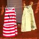 Two dresses hanging on a clothesline. A red and white striped sleeveless dress that has been painted with Minnie Mouse, and a yellow and white striped sleeveless dress painted with Hello Kitty.