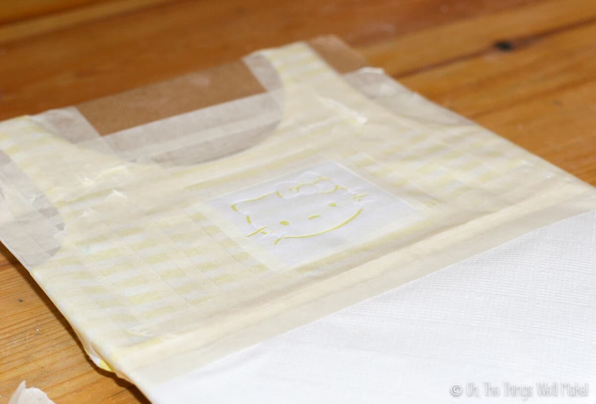 Close up of a Hello Kitty stencil on a yellow and white striped dress, surrounded by masking tape.