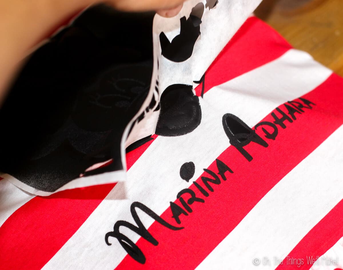 Peeling off a freezer paper stencil, revealing the painted name, Marina Adhara, written in black paint.