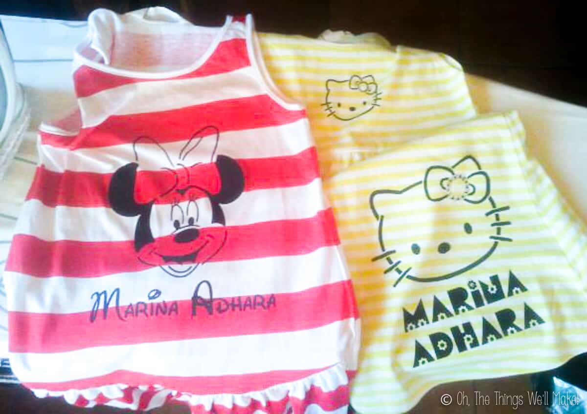 Two dresses placed side by side. On the left is a red and white striped sleeveless dress that has been painted with Minnie Mouse. On the right is a yellow and white striped sleeveless dress painted with Hello Kitty.