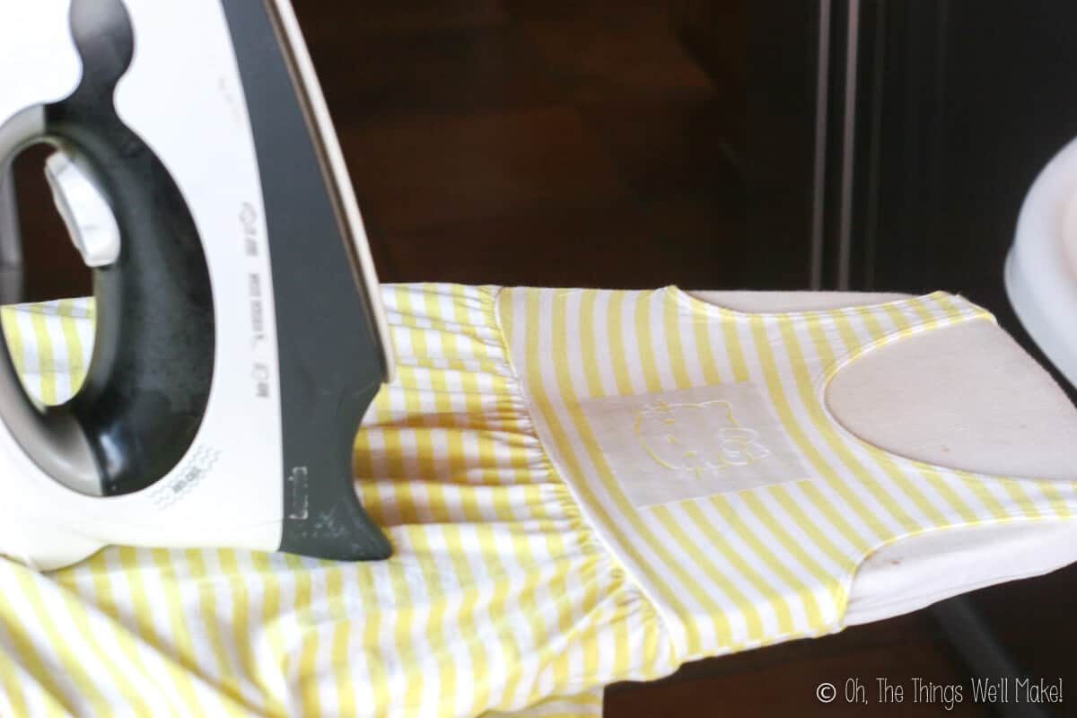 Yellow and white striped sleeveless dress laid on an ironing board with a Hello Kitty freezer paper stencil on it and an iron on the side.