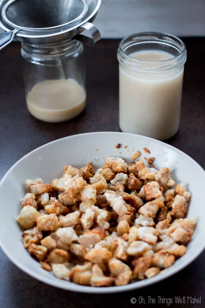 Close up of a white bowl of fried pork cracklings in front of jars of home rendered lard.