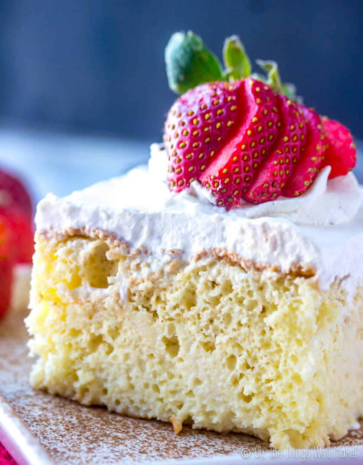 A slice of Tres Leches cake with sliced red strawberries on top.