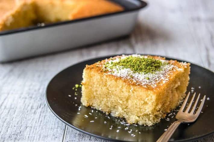 A slice of Greek Revani cake in front of a pan of it.