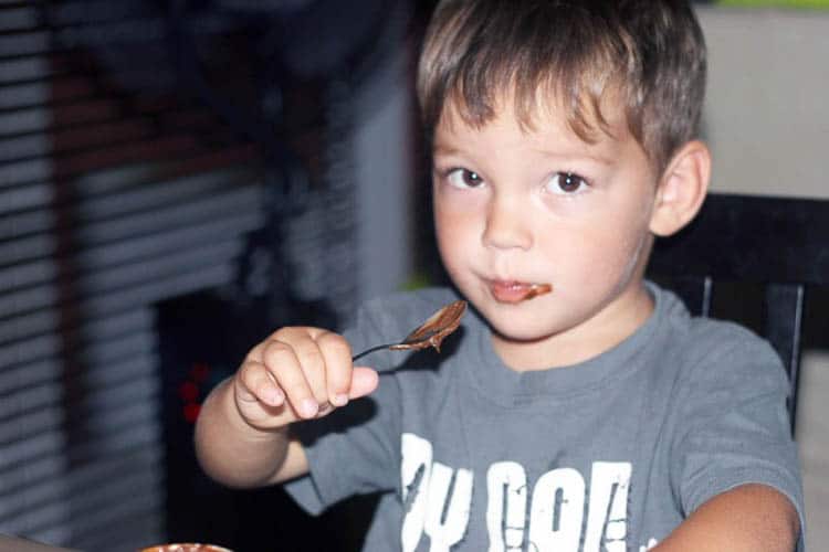 A little boy eating chocolate mousse.