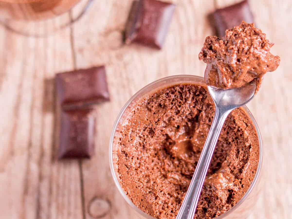 Overhead view of a spoonful of chocolate mousse on top of a jar full of the same mousse with pieces of chocolate scattered around