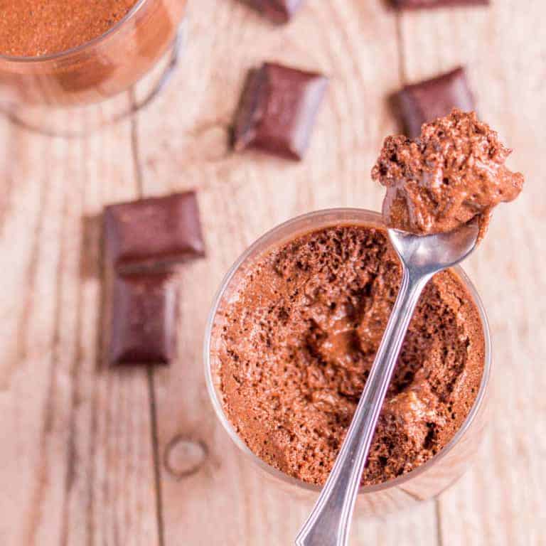 Overhead view of a spoonful of chocolate mousse on top of a jar full of the same mousse with pieces of chocolate scattered around