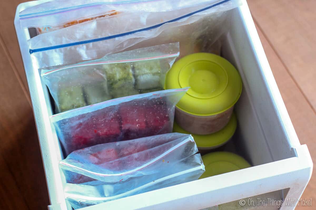 Top view of a freezer drawer full of ziplock bags filled with different fruit ice cubes