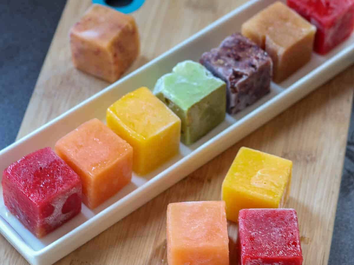 A rainbow of fruit ice cubes laid on a white rectangular plate, ready for making into smoothies