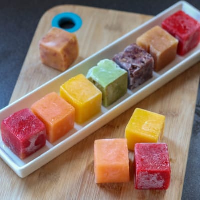 A rainbow of fruit ice cubes laid on a white rectangular plate, ready for making into smoothies