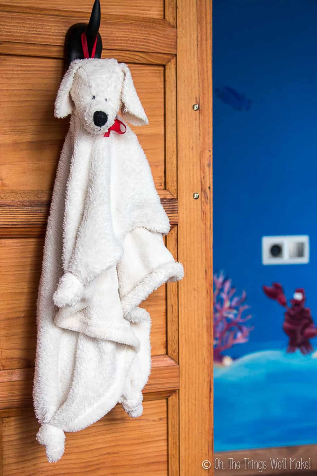 A white fluffy puppy blanket with a stuffed puppy head hanging from the hook on a wood closet door.