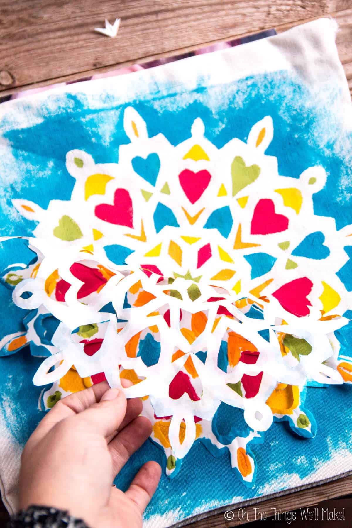 Peeling off the freezer paper snowflake stencil to reveal a beautiful mandala painted on a fabric bag.