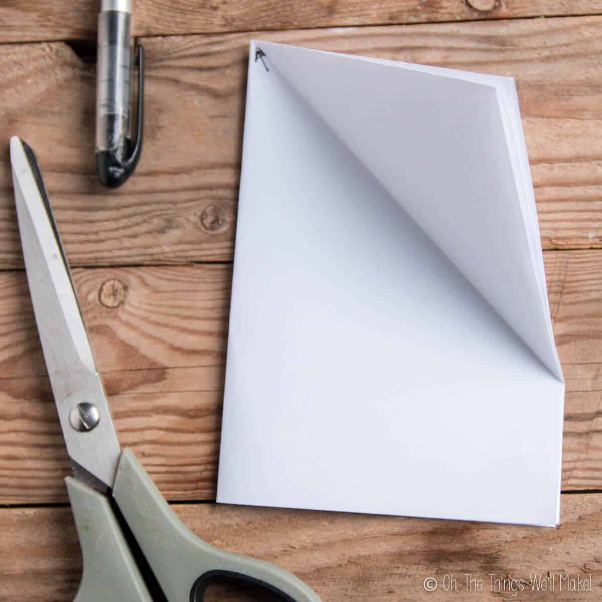 A piece of paper that has been folded in half twice and then marked in the center point with an arrow for further folding for a paper snowflake.