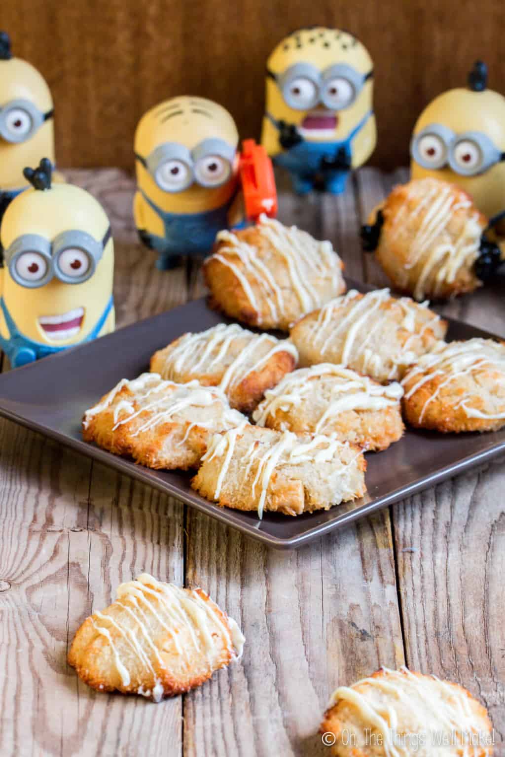 Several minion toys overlooking a black plate full of homemade coconutties  cookies (a mix of macaroons and white macadamia nut cookies) drizzled with white chocolate.