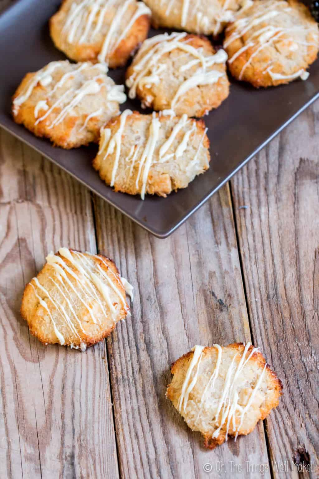 Top view of a black plate full of coconutties cookies (a mix of macaroons and white macadamia nut cookies) with with two pieces laid on the wood surface. 