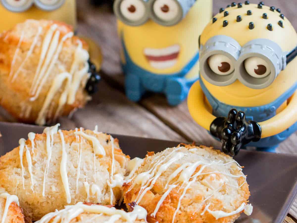 A closeup of delicious coconutties drizzled with white chocolate on a black plate, surrounded by small Minion toys.