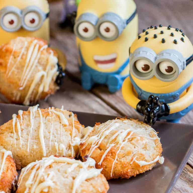 A closeup of delicious coconutties drizzled with white chocolate on a black plate, surrounded by small Minion toys.