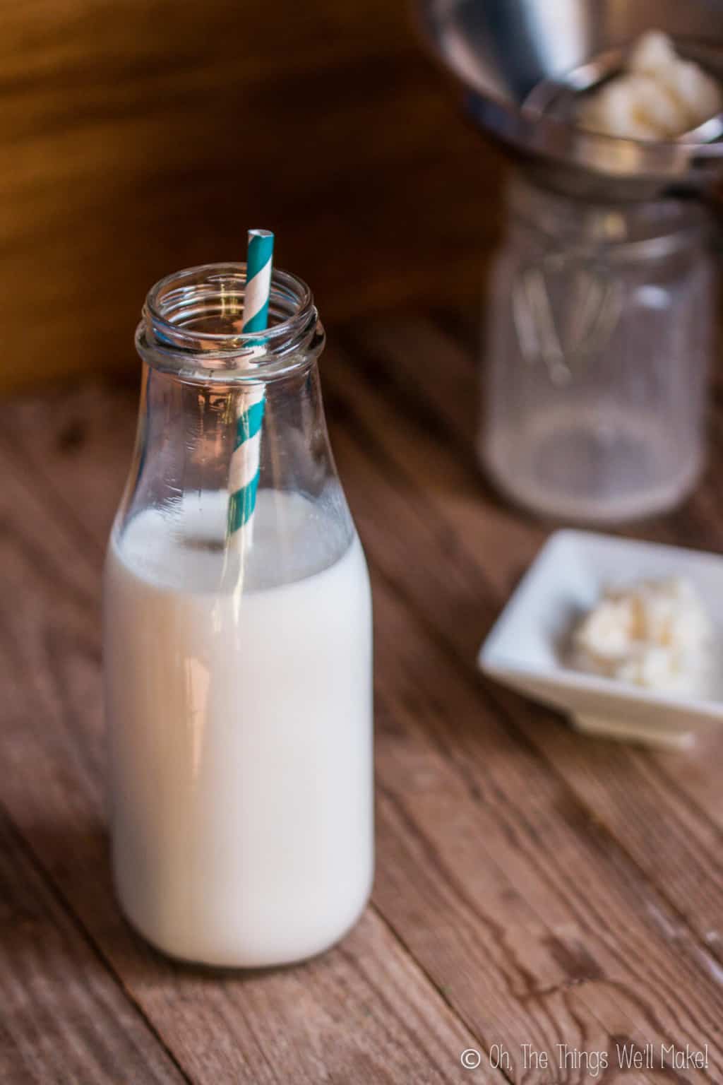 A bottle of kefir with a white and blue striped paper straw in it, next to some kefir grains