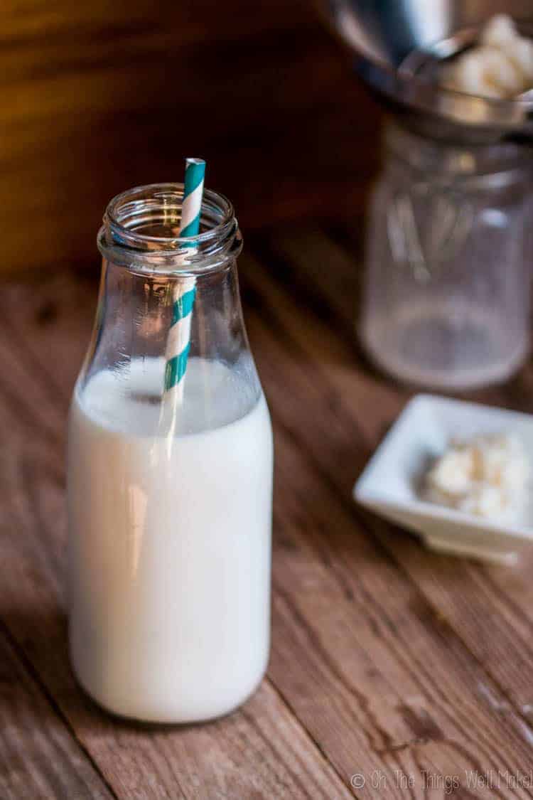 Uma garrafa de kefir com uma palha de papel ao lado de alguns grãos de kefir