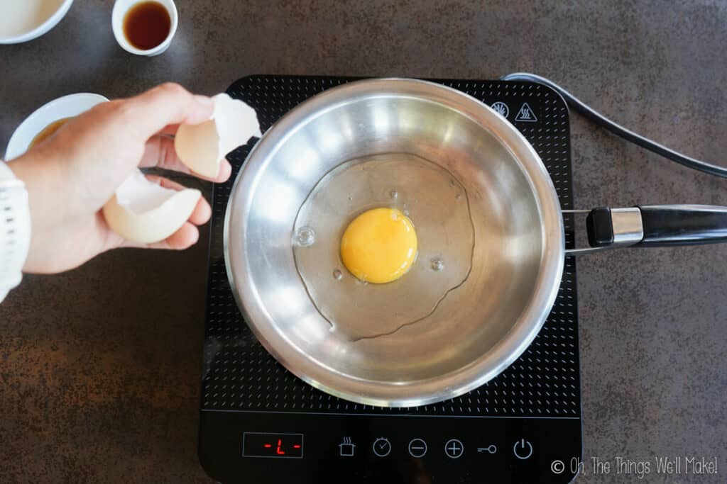 Adding an egg to a stainless steel pan.