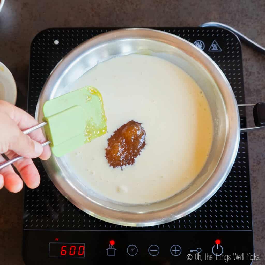 Adding honey to a cream custard mixture in a stainless steel pan.