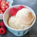 Closeup of 2 scoops of homemade kefir ice cream, or frozen kefir, in a blue bowl, garnished with red raspberries.