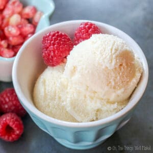 Closeup of 2 scoops of homemade kefir ice cream, or frozen kefir, in a blue bowl, garnished with red raspberries.