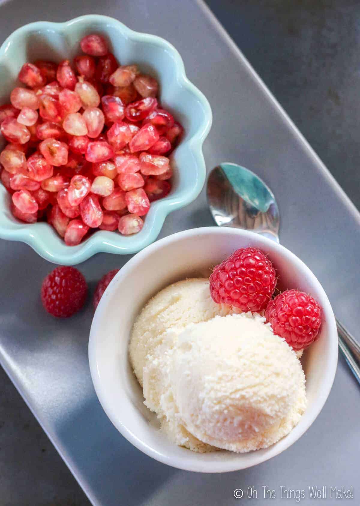 Overhead view of two bowls, one with a homemade frozen kefir ice cream garnished with raspberries. The other is filled with pomegranate seeds.