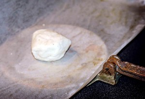 A tortilla press lined with parchment paper and a bowl of dough in the center.